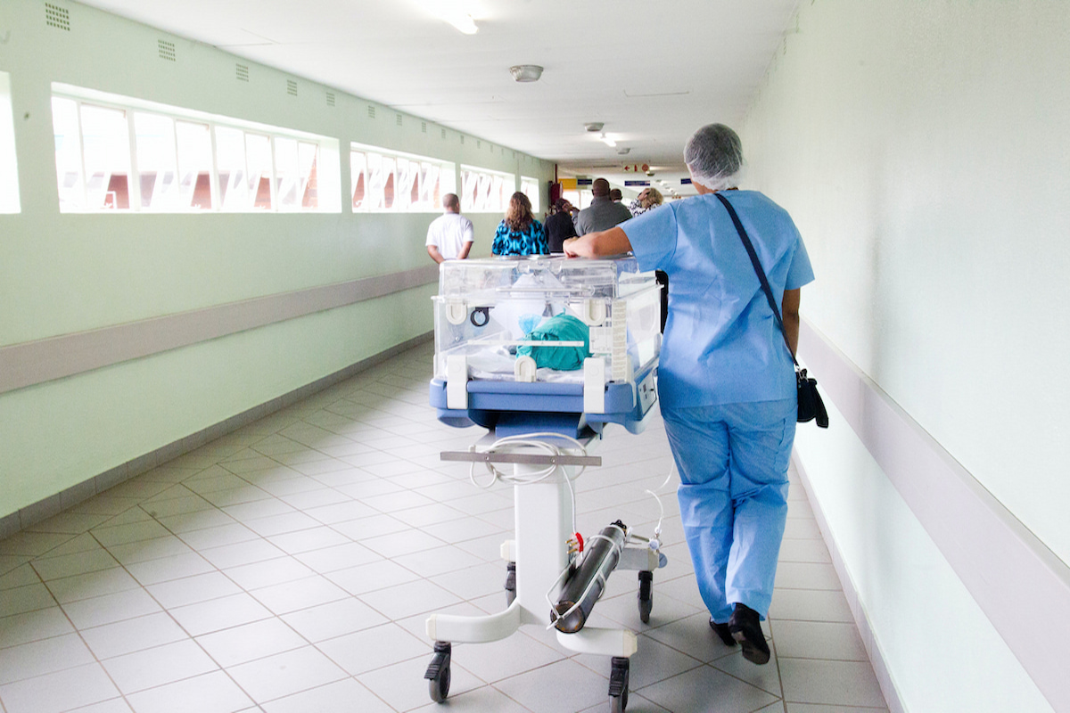 Nurse walking down a hallway rolling a hospital bed along the ground