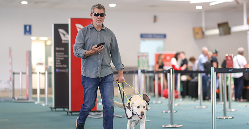 Man with guide dog walks through airport using BindiMaps wayfinding app