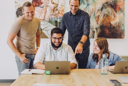 Group of people huddled around a laptop working together. Group of people huddled around a laptop working together.