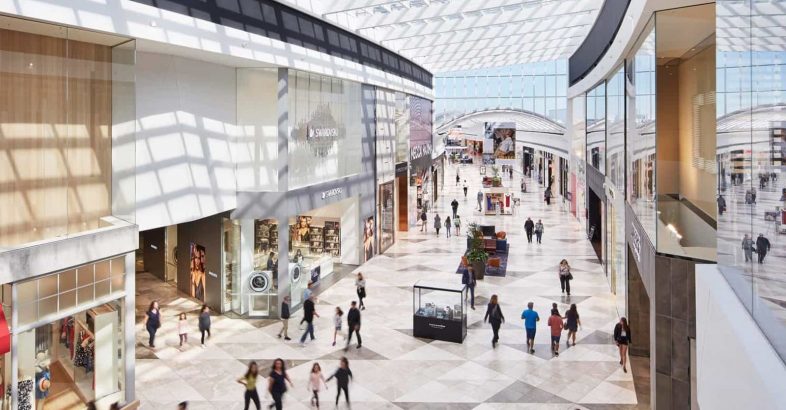 Beautifully lit photograph from a higher angle of the inside of Pacific Werribee shopping centre- glass diamond shaped ceiling panels and marble mozaic floor with people walking around shopping.